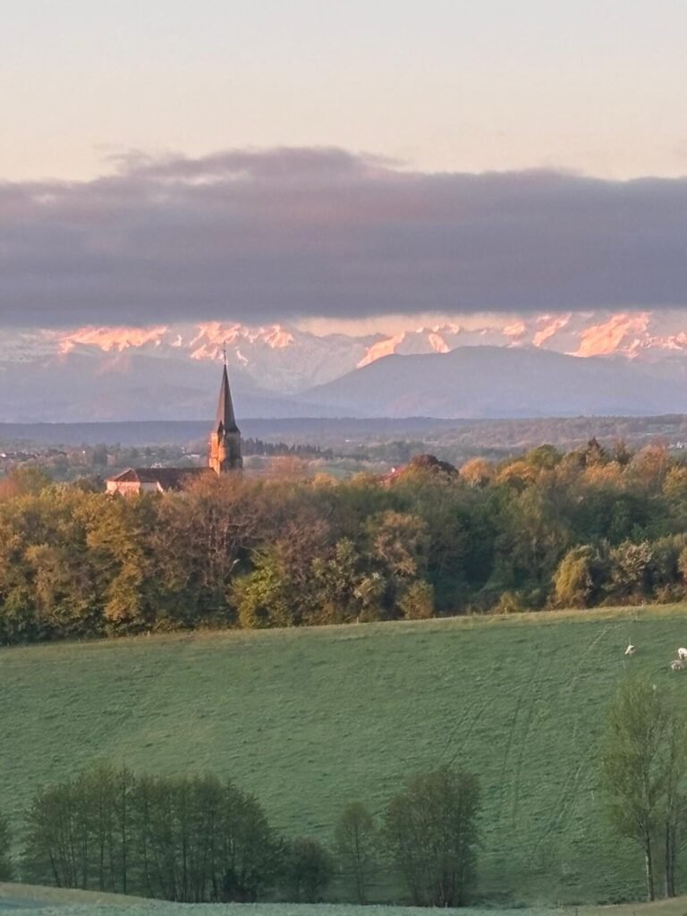 Uitzicht op de besneeuwde Pyreneeën met dorpskerk vanaf Gite La Grange in de Gers